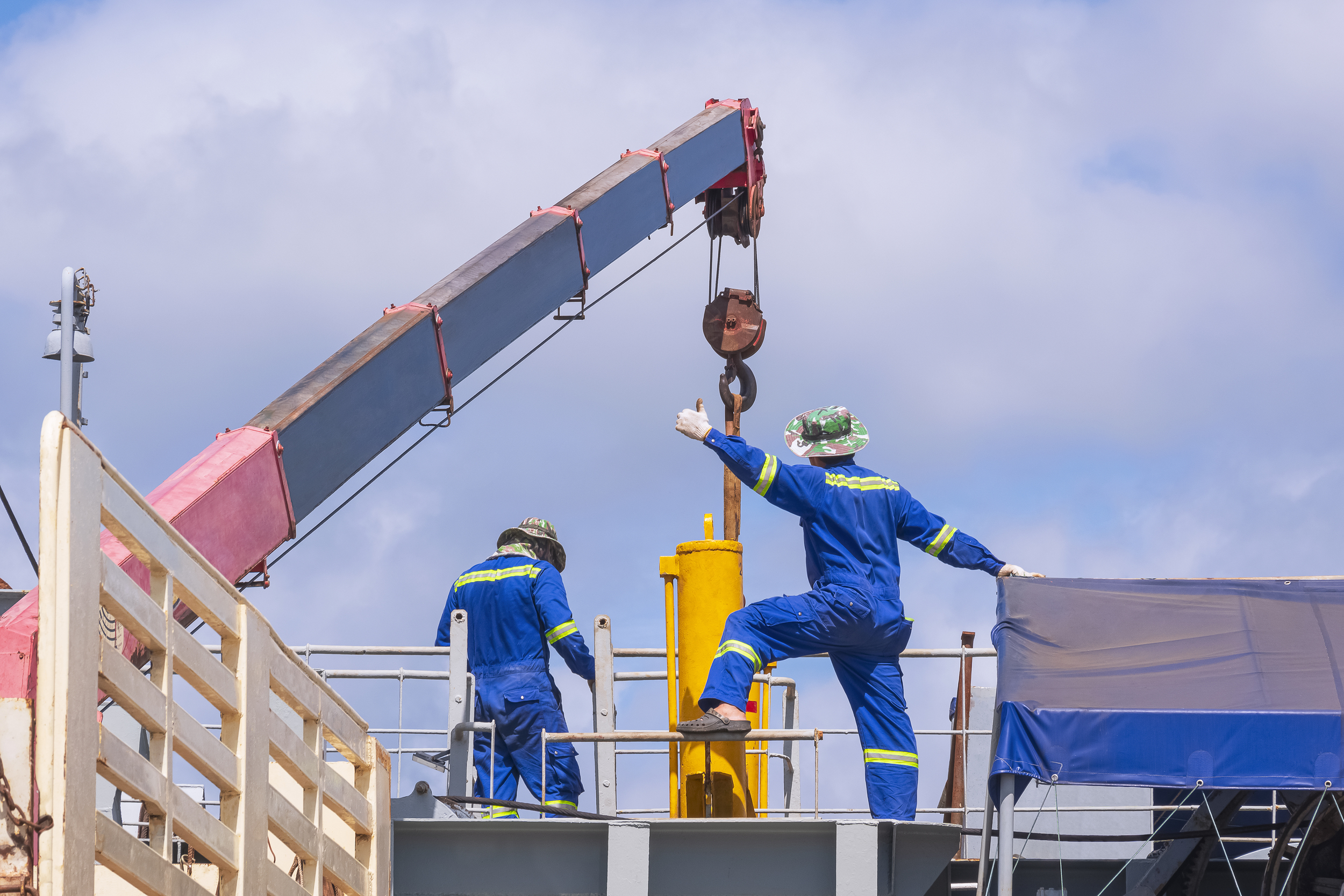 Engineers with crane truck transfer yellow hydraulic cylinder into sand suction dredger ship at harbor to illustrate Hydra-Power Systems Careers